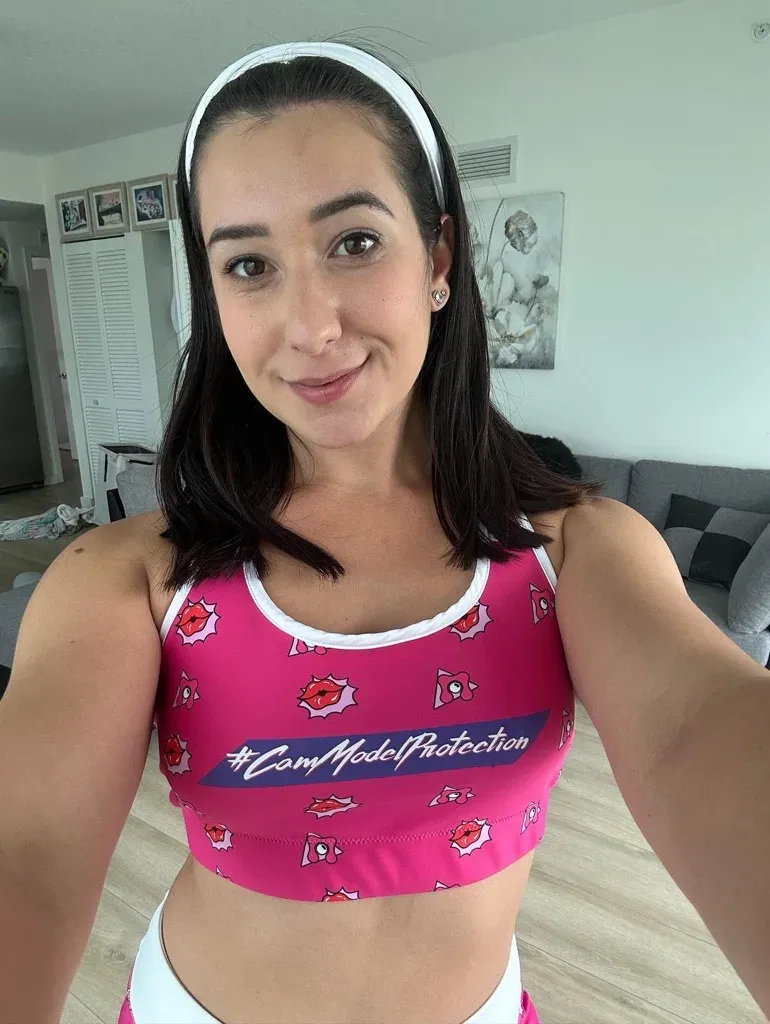 Desy Gato taking a mirror selfie in a pink Cam Model Protection top